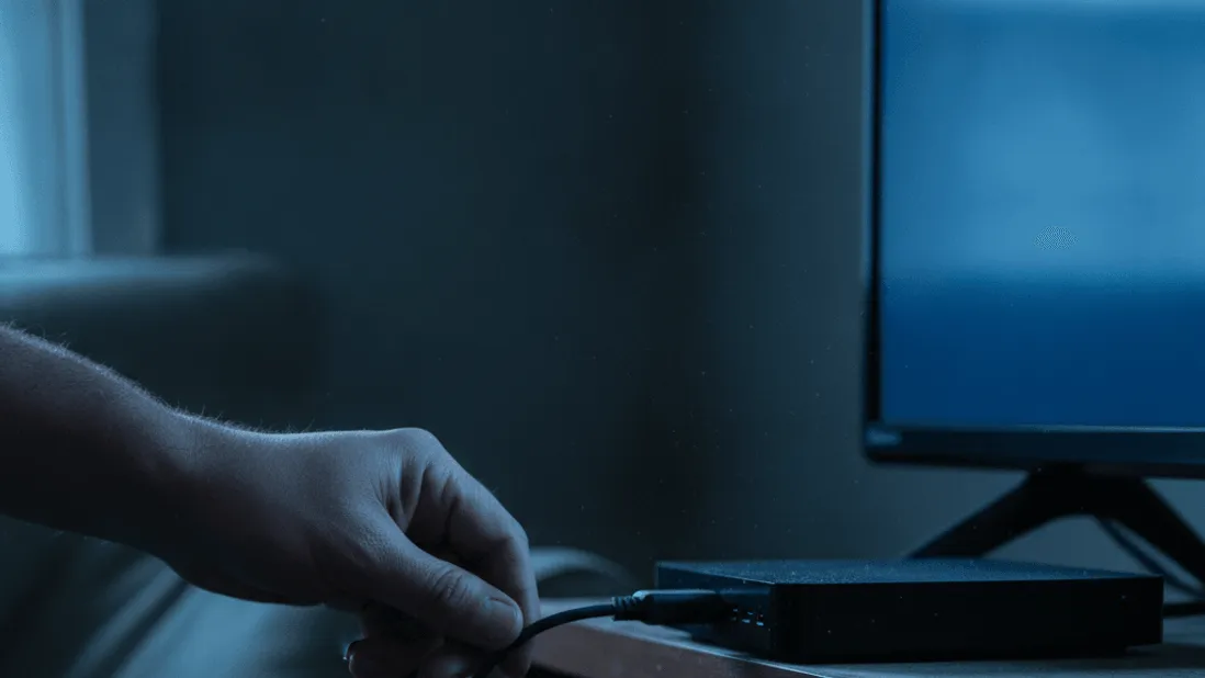 A hand connects a streaming box to a TV, with dust visible in the ambient light.