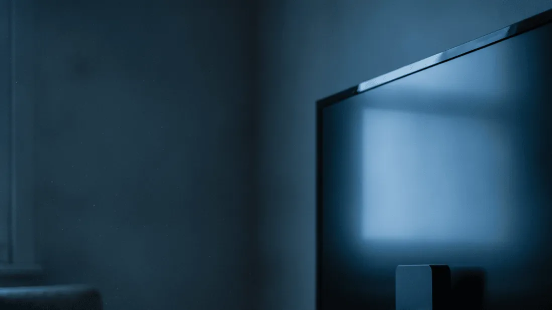 A streaming stick is plugged into a television, with cables and a remote on a wooden shelf, in a dimly lit room.